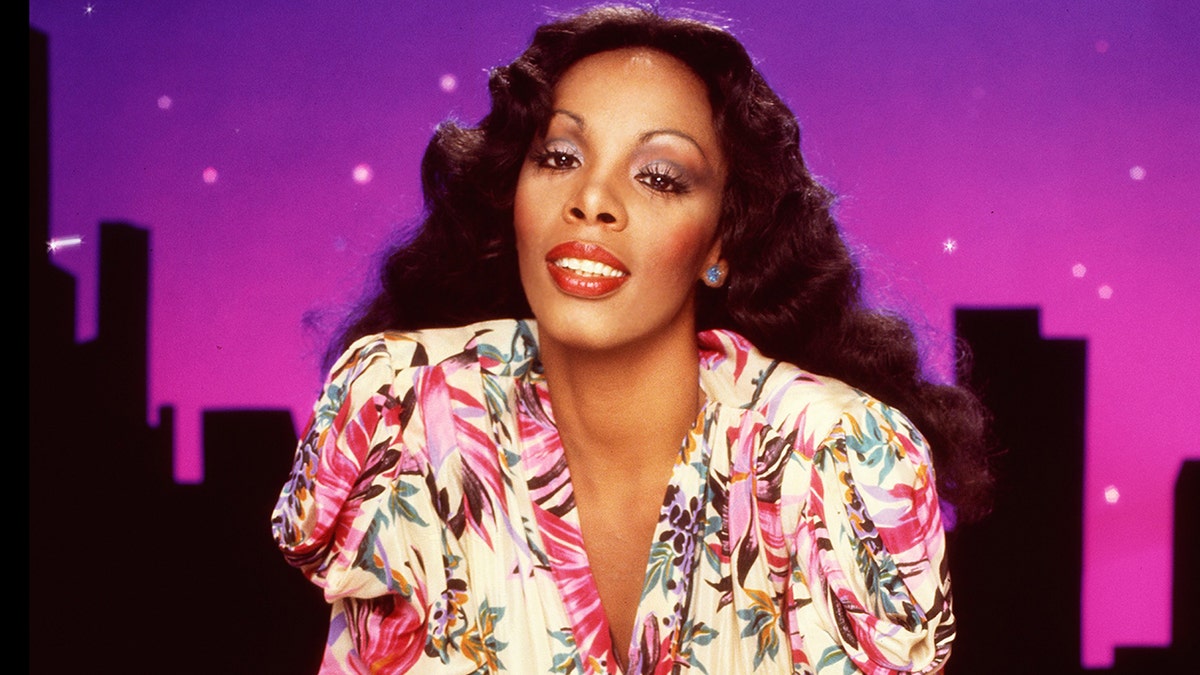 Een close-up van Donna Summer die voorover leunt en een bloemenjurk draagt