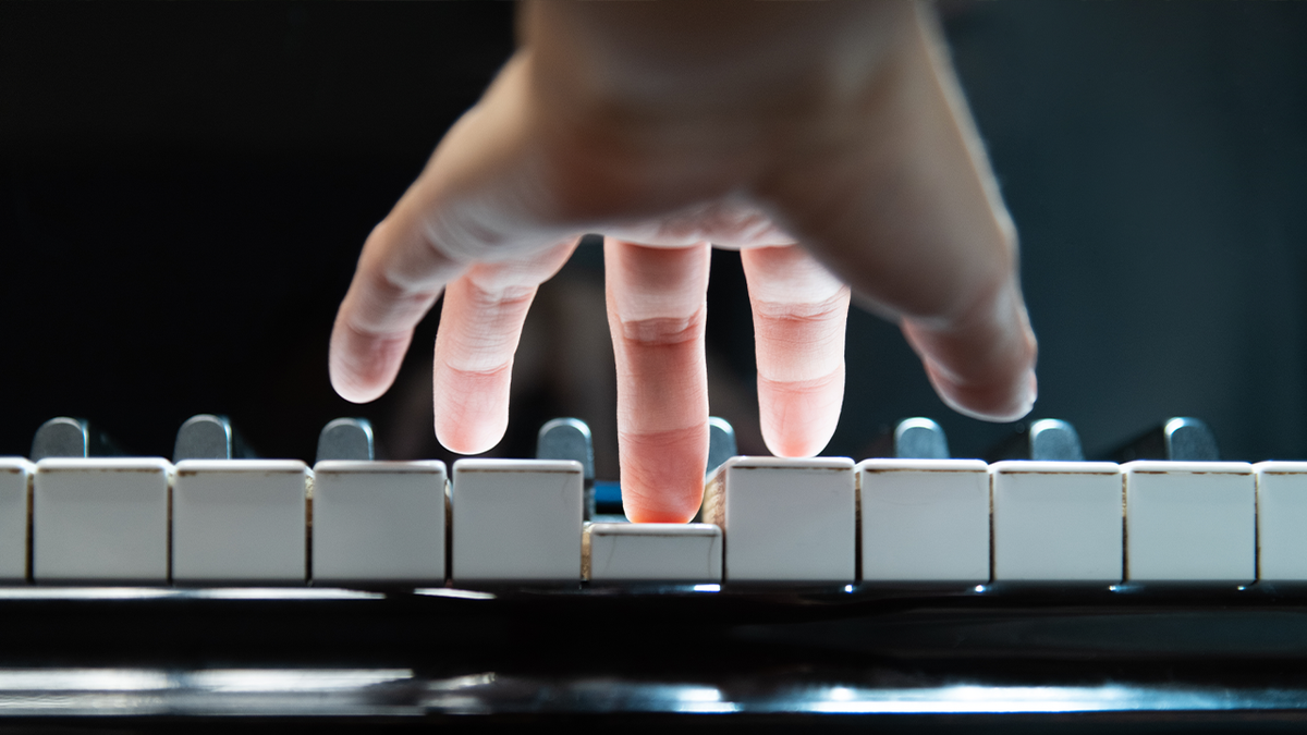 Een hand boven een pianoklavier, die met de middelvinger op een toets drukt