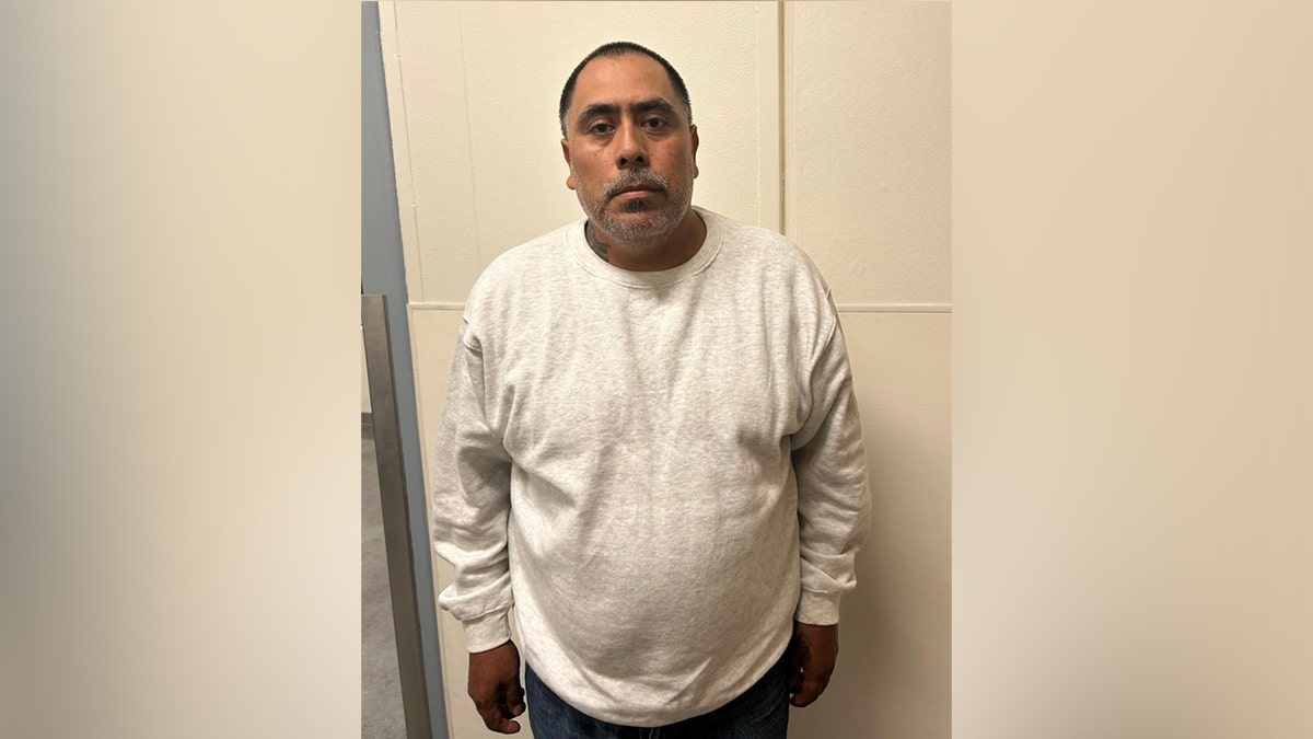 Een illegale landarbeider poseert voor een boekingsfoto in een wit shirt met lange mouwen