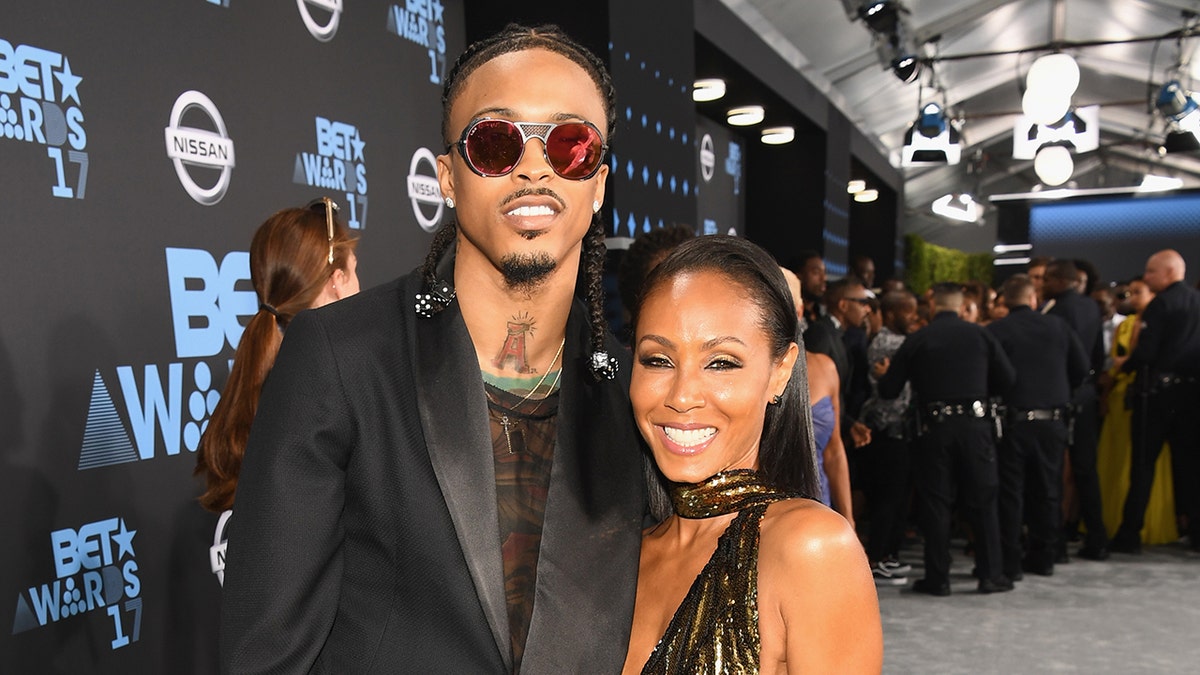 August Alsina en Jada Pinkett Smith glimlachen terwijl ze allebei een zwarte outfit dragen