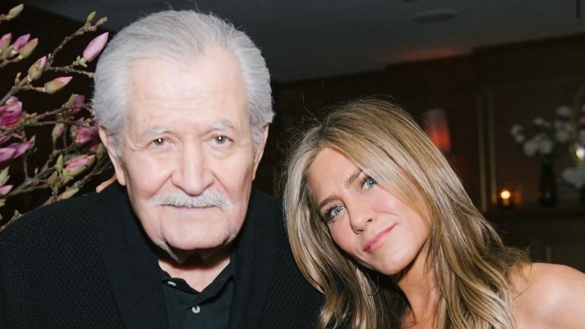 Jennifer Aniston in een zwarte outfit buigt haar hoofd naar vader John, ook in het zwart