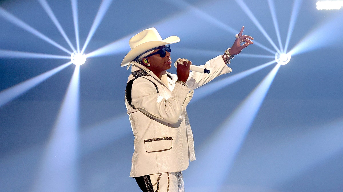 Jimmie Allen treedt op het podium op in een wit pak en cowboyhoed