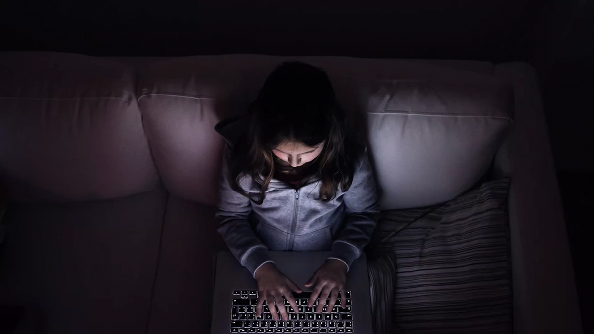 Klein meisje, zittend in het donker, spelend met laptop .